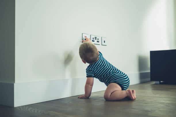 A little baby is reaching for a plug socket at home not knowing the danger
